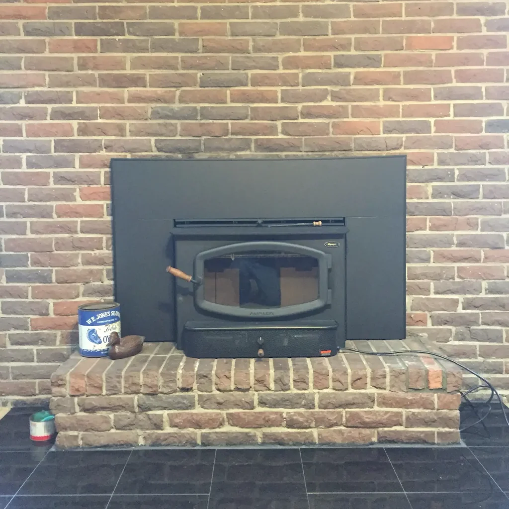 Clean and ready wood stove insert in Chesapeake, VA, professionally vented and mounted within a brick fireplace.