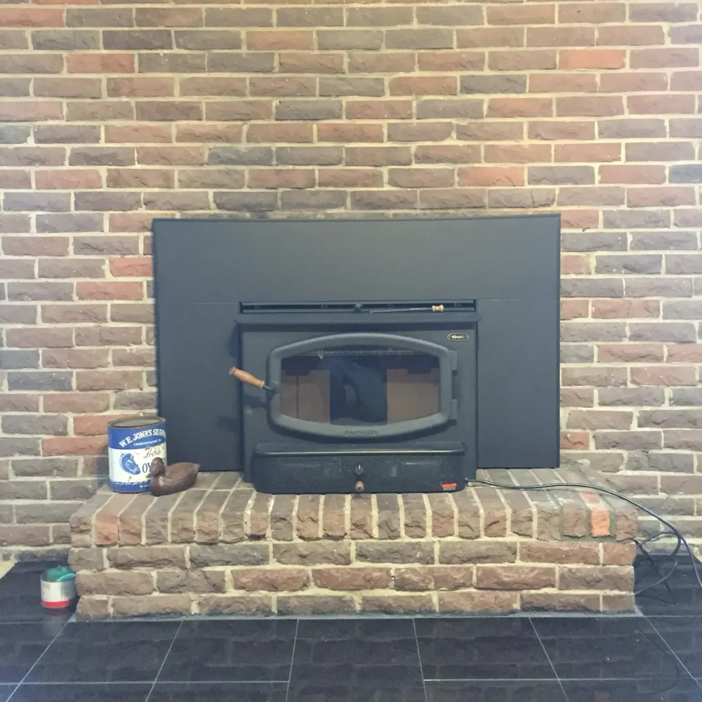 Clean and ready wood stove insert in Chesapeake, VA, professionally vented and mounted within a brick fireplace.