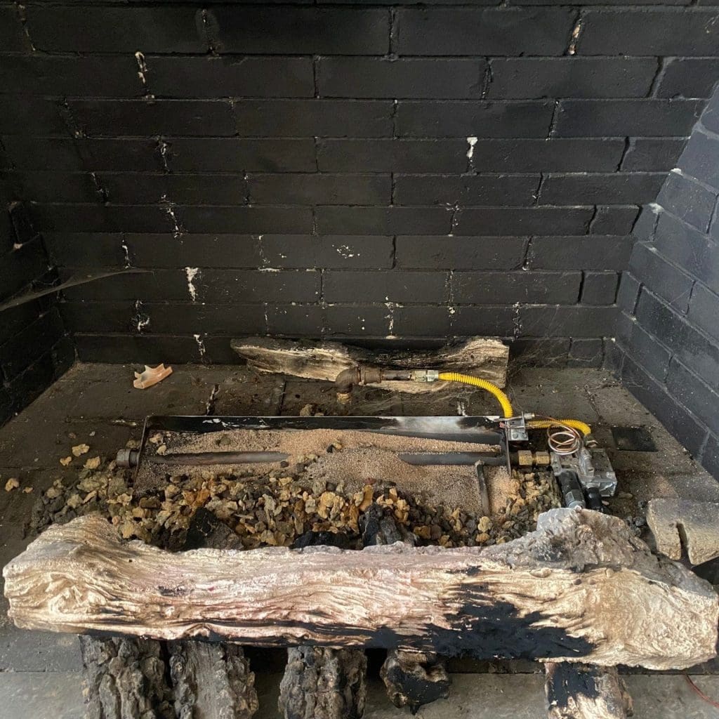 Old gas fireplace with outdated gas logs and worn firebox interior, photographed before professional gas fireplace repair by Premier Chimney and Roofing.